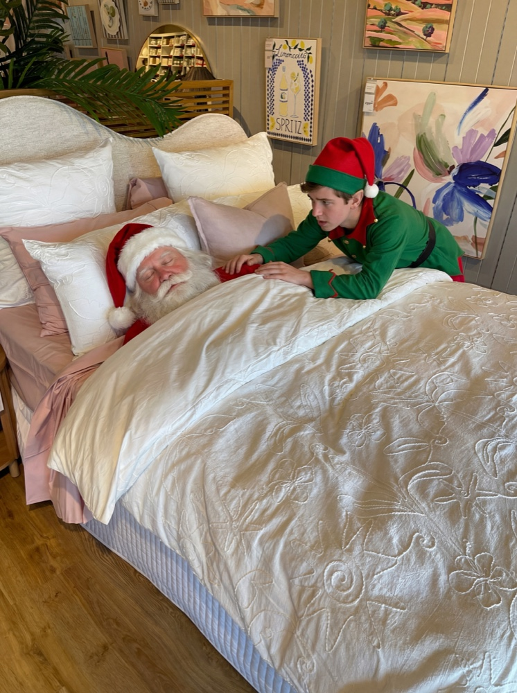 Santa taking a nap with an elf trying to wake him